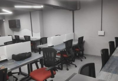Shared workspace area featuring desks with privacy dividers and overhead linear lighting.