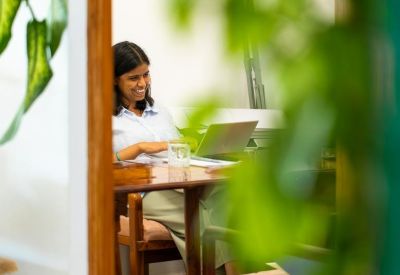 Member working on a laptop at a wooden desk framed by lush green plants.