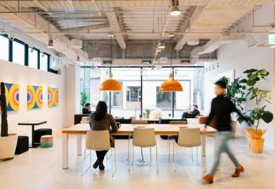 Bright open-plan workspace featuring a long wooden communal table and orange pendant lights.