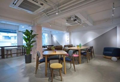 Spacious communal lounge with diverse seating, wooden tables, and a large potted plant.