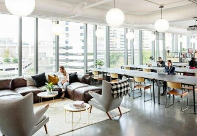 Bright coworking lounge with large windows, leather sofas, and long communal tables.