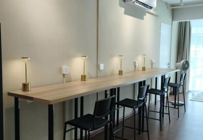 Long wooden high-top desk with bar stools and individual task lighting against a neutral wall.