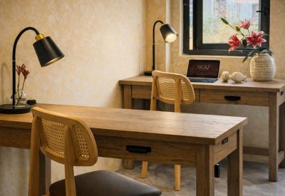 Wooden workstation with a black desk lamp, wicker chair, and pink lilies in a vase.
