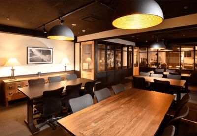 Large conference room with multiple dark wood tables, grey chairs, and pendant lighting.