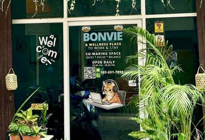 Glass entrance of BonVie Sathorn decorated with hanging vines and a welcome sign.