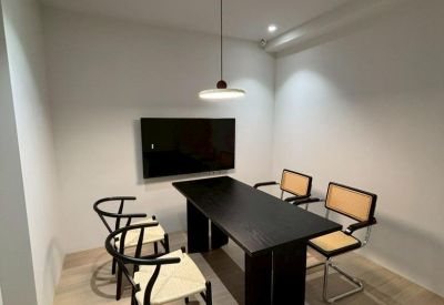 Minimalist conference room with a black table, wishbone chairs, and a wall-mounted screen.