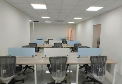 Bright workspace featuring rows of desks with blue and white privacy dividers and chairs in protective wrapping.