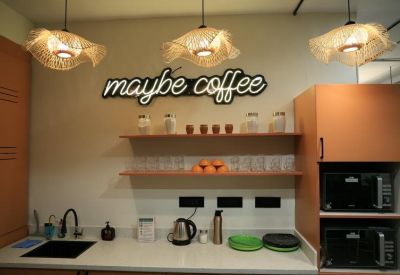 Office kitchen area named Maybe Coffee with wooden shelves, hanging basket lights, and modern appliances.