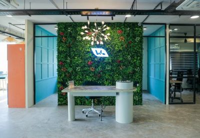 Reception desk backed by a green plant wall with the company logo and a designer sputnik chandelier.