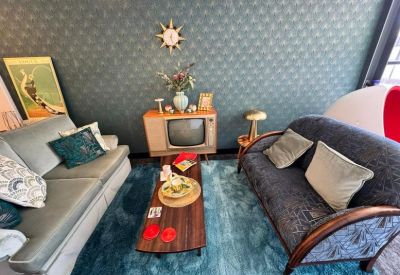 Vintage-style breakout area with blue patterned wallpaper, mid-century furniture, and a blue rug.