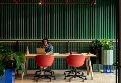 Coworking space with a person working at a wooden table against a green slatted wall.