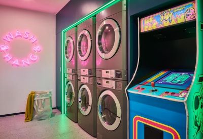 Laundry room with industrial washers, neon signage, and a retro arcade machine.