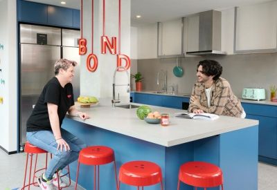 Communal kitchen with blue island, red stools, and hanging red letter decor.