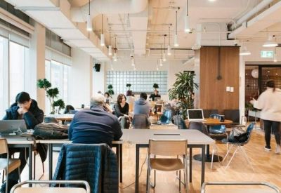 Bright coworking space with shared wooden tables, ergonomic chairs, and large windows.