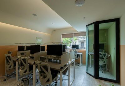 Bright office with multiple ergonomic workstations and a glass-walled phone booth.