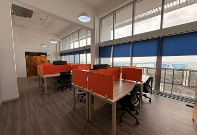 Spacious office layout with several wooden desks, orange dividers, and blue window blinds.