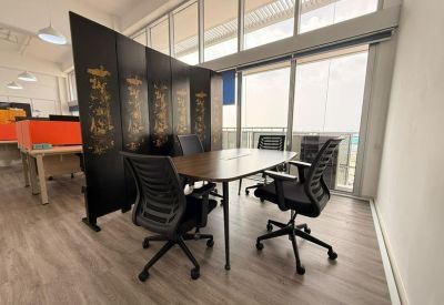 Modern meeting space with a wood-finish table and black ergonomic chairs near a large window.