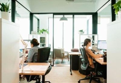 Bright glass-walled office with individuals working at modern desks.