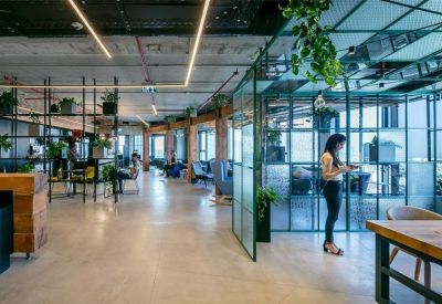 Open-plan office space with industrial ceilings, indoor plants, and glass partitions.