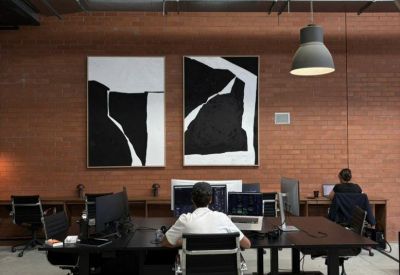 Spacious open-plan office with brick walls, large abstract art, and individual computer workstations.