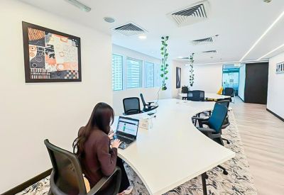 Open-plan office with a woman working at a large white curved communal table.