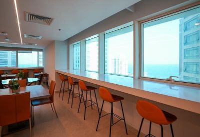 Modern office dining area with a long window-facing breakfast bar and orange high stools.