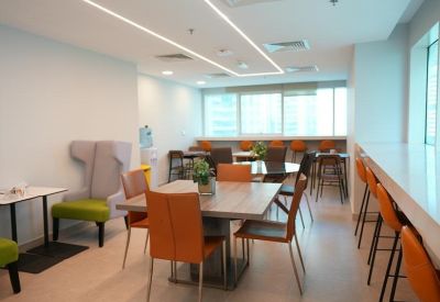 Vibrant communal kitchen and lounge area with wooden tables and colorful orange chairs.