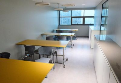 Long communal dining or training area with yellow tables and grey chairs near large windows.