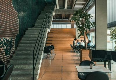 Spacious communal lounge with a concrete staircase, brick accents, and a large indoor tree.