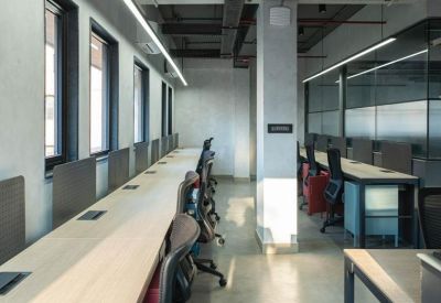 Bright open-plan office with long wooden desks and ergonomic black chairs.