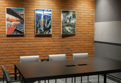 Meeting room featuring a long black table, grey chairs, and a red brick accent wall with framed art.