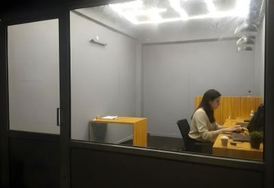 Private office suite seen through a glass partition, featuring a minimalist desk and bright overhead lighting.