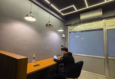 Modern coworking area featuring a long wooden desk, pendant lighting, and a black ceiling with linear LEDs.