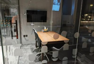 Modern glass-walled private office featuring a wooden desk and black ergonomic chairs.