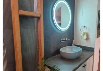 Stylish restroom featuring a vessel sink on a wooden vanity and a circular backlit mirror.