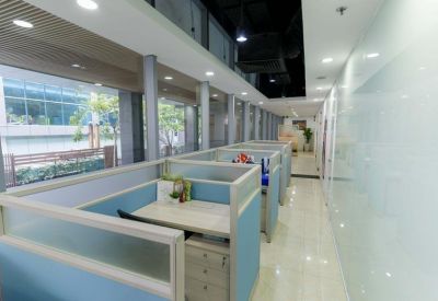 Quiet office workstation aisle with blue-paneled cubicles and large windows overlooking the street.