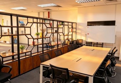 Large meeting room featuring a long light wood table, black mesh chairs, and a whiteboard.