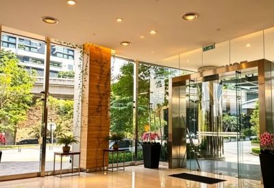 Spacious sunlit lobby with glass entrance doors, indoor plants, and polished floors.