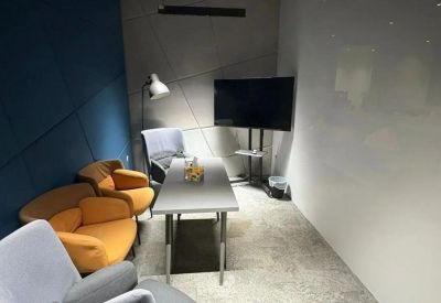 Compact meeting space with a whiteboard wall, grey and orange lounge seating, and a flat-screen monitor.