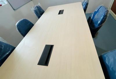Meeting room with a large table, power sockets, and blue chairs still in plastic wrap.
