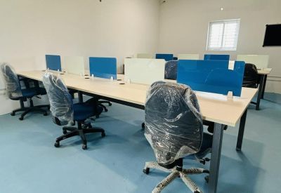 Open-plan office area featuring light wood desks and ergonomic chairs with protective covering.