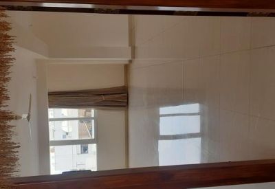 A wooden-framed mirror reflecting a room with a window and white walls.