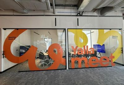 Glass-walled conference rooms featuring vibrant orange and yellow Yalla meet graphics.