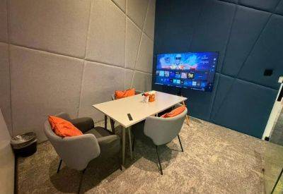 Modern meeting space featuring grey tub chairs with orange accent pillows and a flat-screen display.