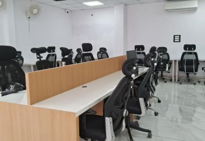 Close-up of a long wooden desk with black office chairs in a bright room.
