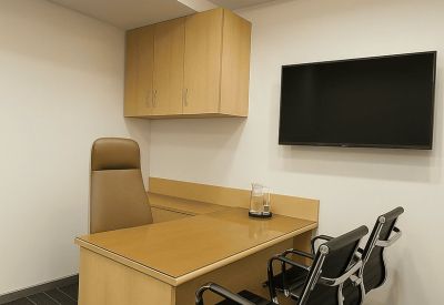Compact consultation room with a wooden desk, two guest chairs, and a wall-mounted TV.