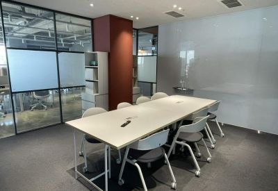 Modern meeting room featuring a long white table, whiteboard wall, and glass partitions.