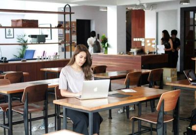 Shared workspace with wooden tables, a woman working on a laptop, and modern shelving.