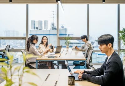 Modern office interior with rows of desks, glass partitions, and industrial ceiling.