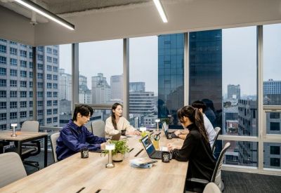 Long wooden coworking table by large windows overlooking the city.